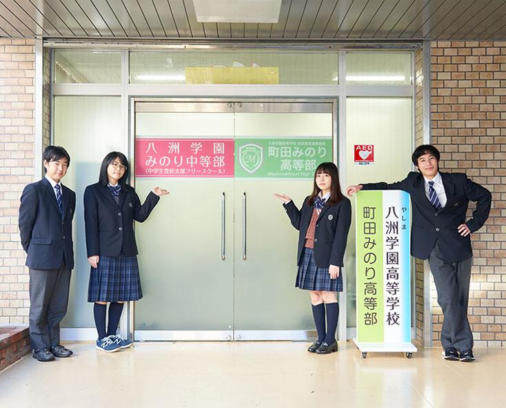 学校の扉の前で生徒4人が並んでいる写真